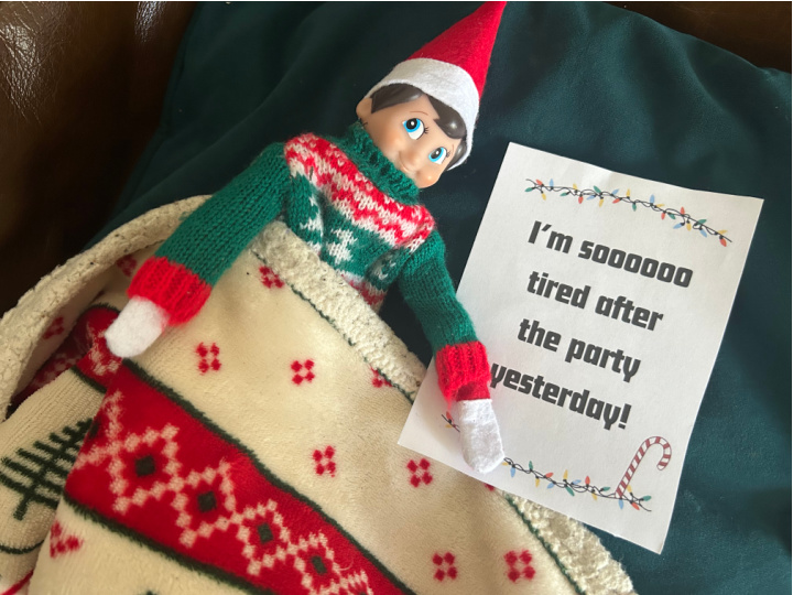 Elf on the Shelf tucked up in bed under a blanket