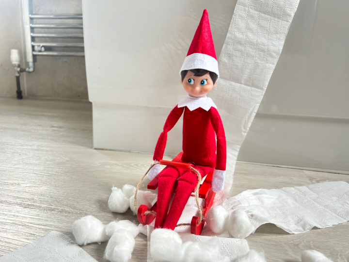elf on the shelf riding a toy toboggan through a bathroom