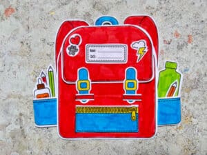 decorating the backpack craft with paper stickers and adding paper school supplies into the side pockets