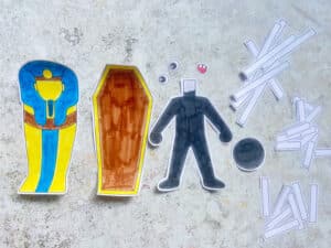 cut out pieces for a halloween mummy craft including the mummy's body, eyes, mouth, paper bandages and a coffin